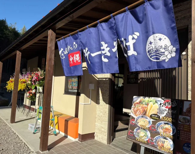 てぃんがーら大谷本店の外観。紺色の暖簾と沖縄そばの看板